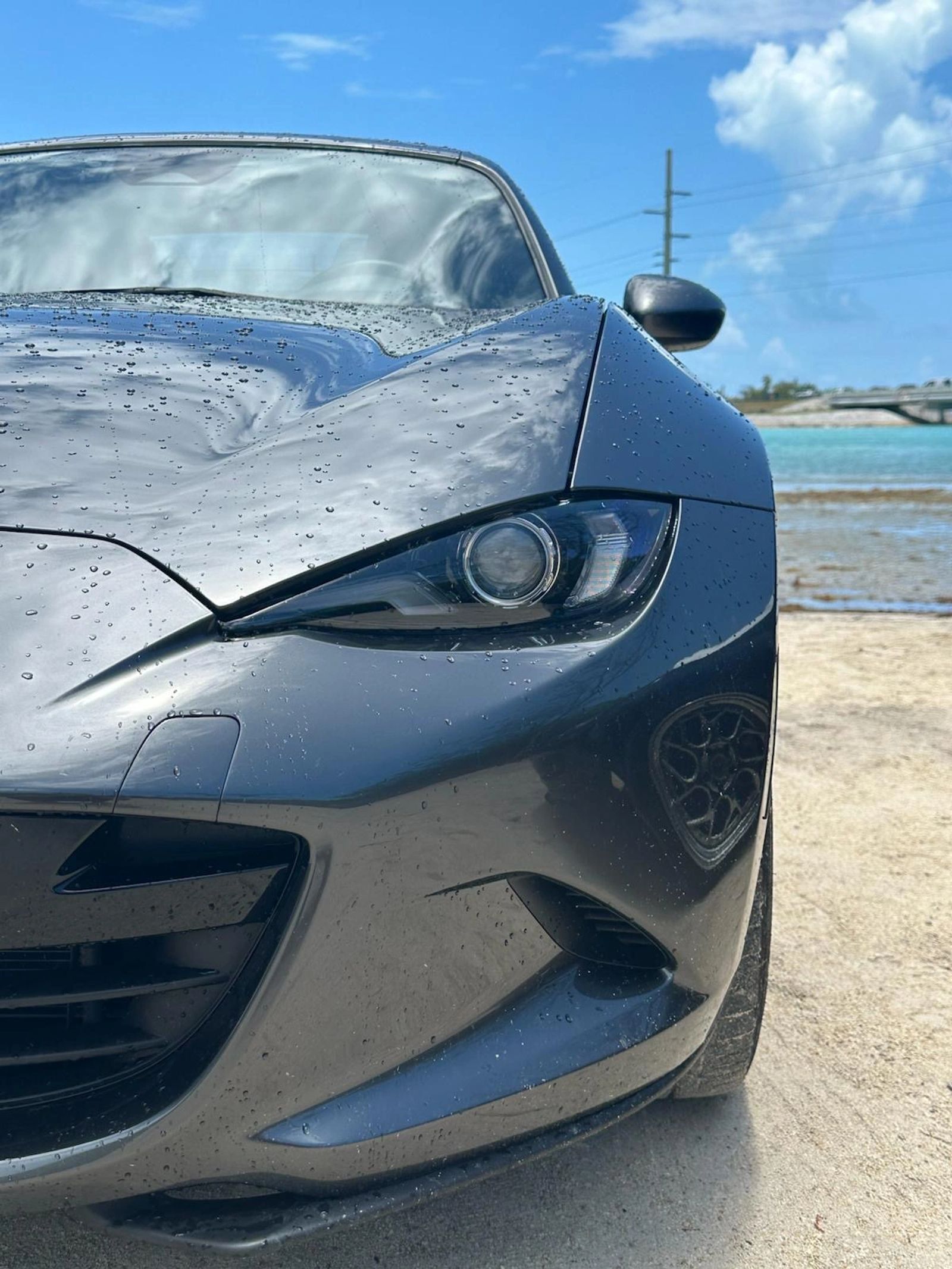 Close-up of a silver Miata beside the water