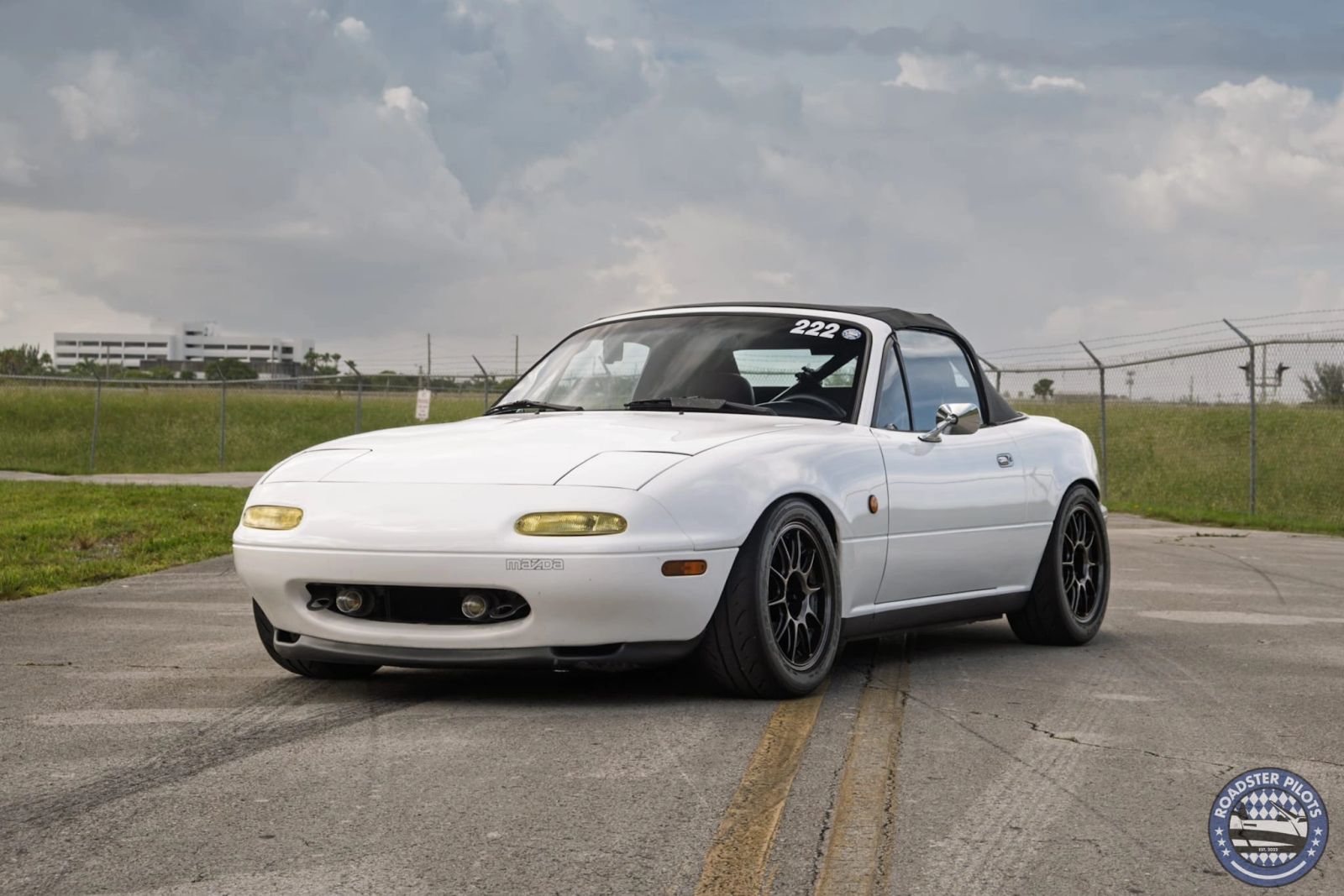 White classic Miata parked beside an open field