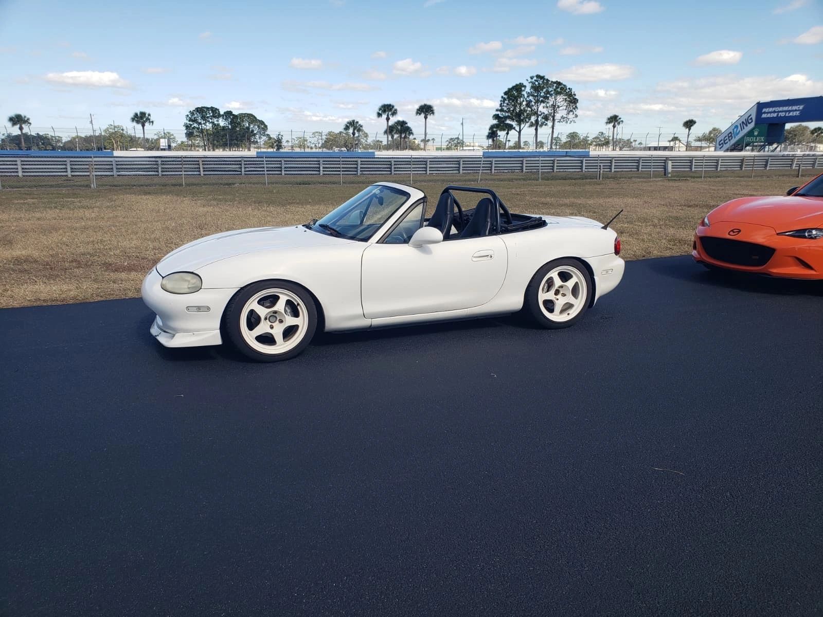 White classic Miata cruising alongside an orange Miata