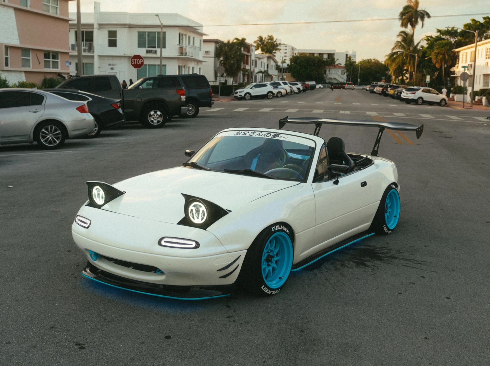 White Miata with pop-up headlights and turquoise wheels