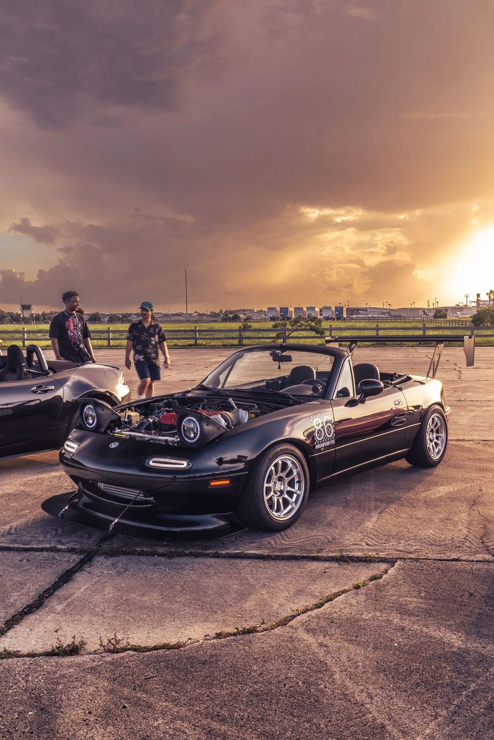 Dark Miata by the water beneath a colorful sunset
